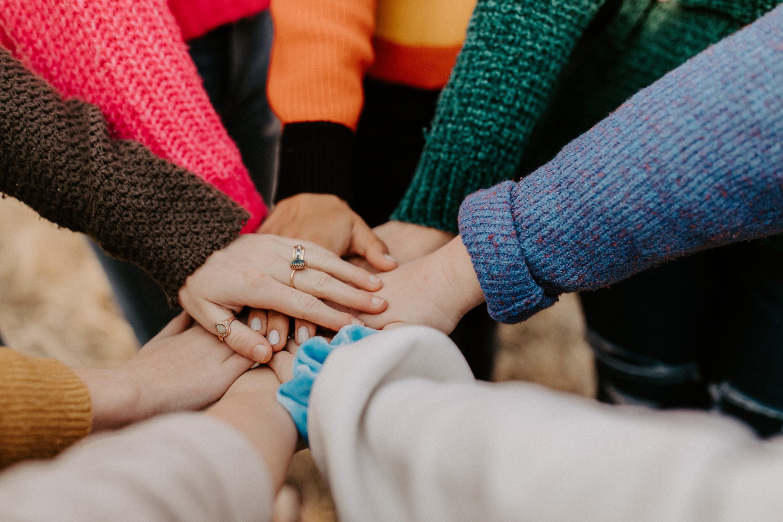 Hands together in colorful sweaters for unity.
