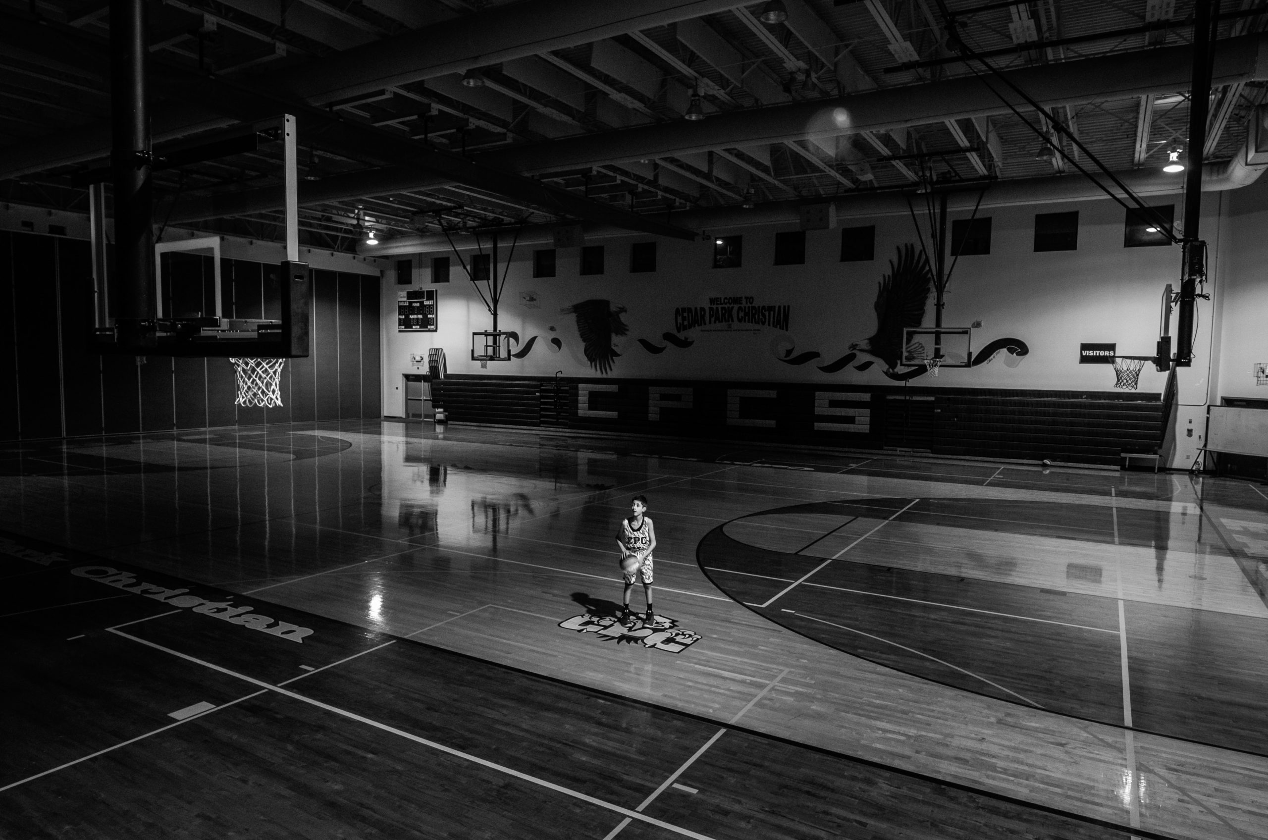 Person standing alone in dark basketball court.